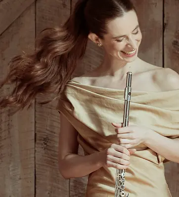 A smiling person holds a metal wind instrument.